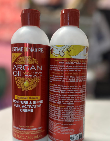 Two bottles of Crème of Nature Argan Oil product on a white surface with a blurred background in Raqlyn store