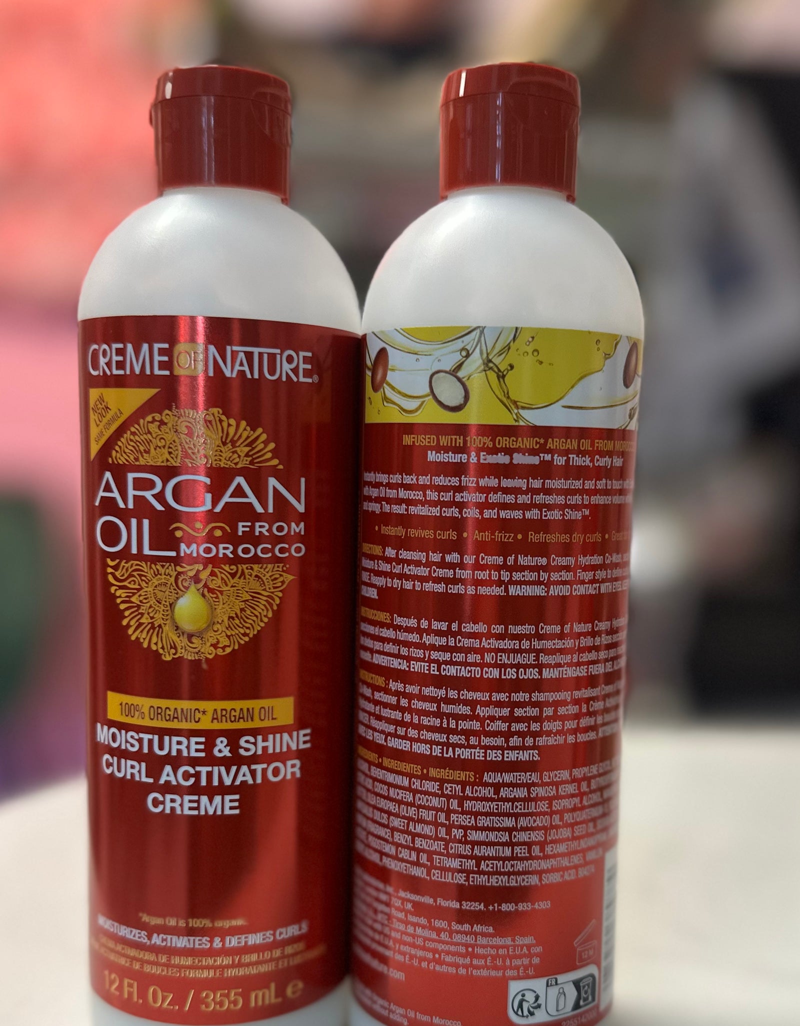 Two bottles of Crème of Nature Argan Oil product on a white surface with a blurred background in Raqlyn store